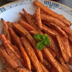 Chrupiące frytki z marchewki, przyprawione i lekko przypieczone, podane na talerzu z natką pietruszki.