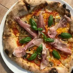 Pyszna pizza z szynką parmeńską i bazylią. Zastanawiasz się, ile kosztuje pizza w Chorwacji? Ta wygląda na wartą swojej ceny!