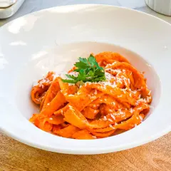 Pappardelle z kremowym sosem z pieczonej papryki, posypane parmezanem i udekorowane natką pietruszki. Pyszne danie, które zachwyca smakiem.