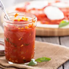 Domowy sos do pizzy z passaty, czosnku i bazylii w słoiku, gotowy do użycia na świeżo upieczonej marghericie.