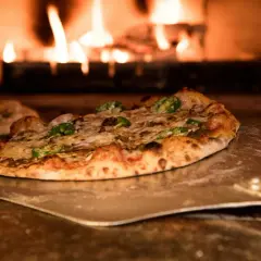 Pizza z pomidorami z puszki, serem i papryczkami jalapeno na łopacie, w tle płomienie pieca.