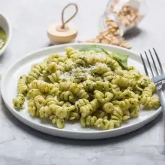 Fusilli z pesto, posypane parmezanem. Na stole kawałek sera, miseczka sosu i słoiczek z orzeszkami pinii. Różne rodzaje makaronu mogą być równie pyszne!
