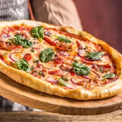Pyszna pizza z rukolą i cebulą na drewnianej desce. Czy pizza jest lekkostrawna? Ta wygląda apetycznie!