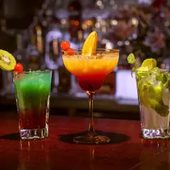Kolorowe drinki na barze: zielony z kiwi i truskawką, pomarańczowo-czerwony z pomarańczą, oraz mojito z miętą i limonką. Idealne na wieczór z **tekila**.