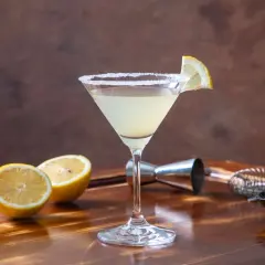 Elegancki drink Martini Bianco z cytryną i solą na kieliszku, obok połówki cytryny i oliwek.