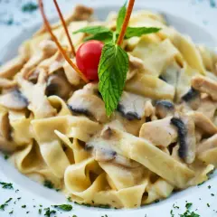 Tagliatelle z pieczarkami i kurczakiem w kremowym sosie, udekorowane pomidorkiem i miętą. Pyszne danie na talerzu.