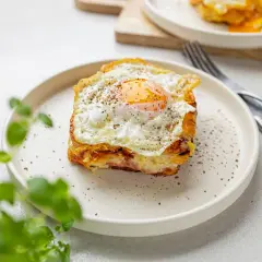 Pyszny croque madame z jajkiem sadzonym na wierzchu, podany na talerzu z pieprzem.
