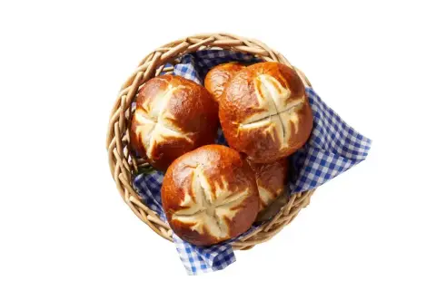 Koszyk z kilkoma świeżymi bułkami bawarskimi, ułożonymi na niebiesko-białej kratkowanej ściereczce.