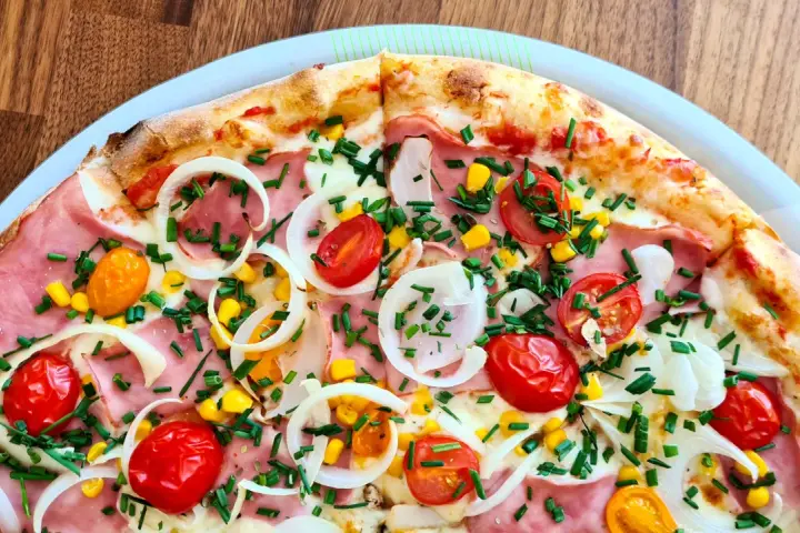 Pyszna pizza 32 cm na ile osób? Ta z szynką, pomidorkami, kukurydzą i cebulą z pewnością zadowoli 2-3 głodomorów.