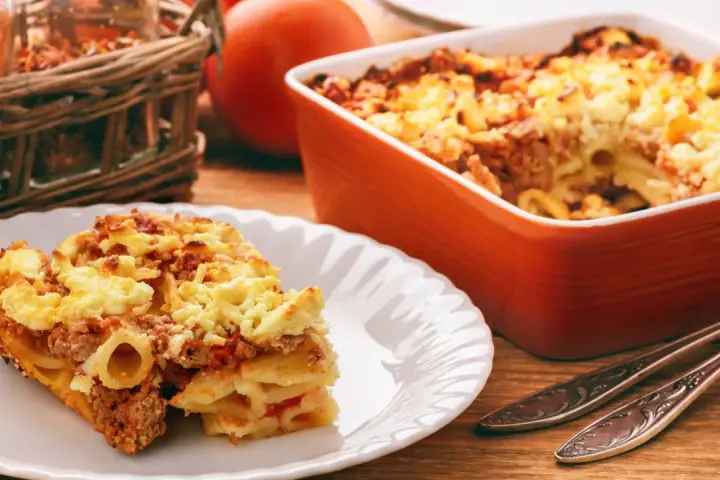 Zapiekanka makaronowa z mięsem mielonym w sosie śmietanowym, podana na talerzu, obok naczynia żaroodpornego.