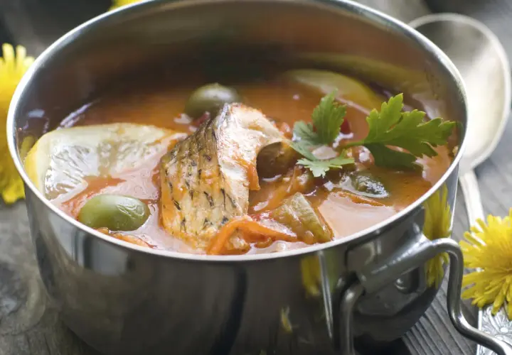 Aromaticzna rosyjska zupa rybna z kawałkami ryby, oliwkami, cytryną i natką pietruszki w metalowej misce.