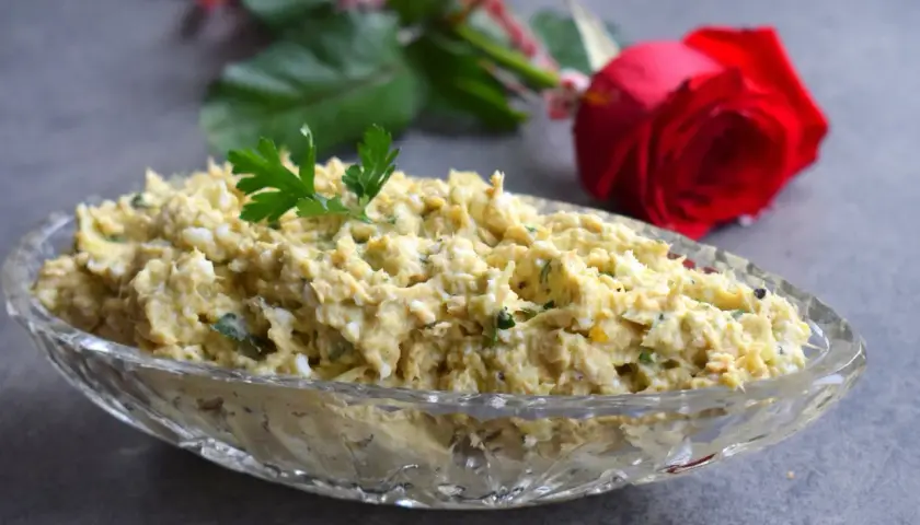 Pyszna pasta z awokado i tuńczyka, udekorowana natką pietruszki, w kryształowej misie. W tle czerwona róża.