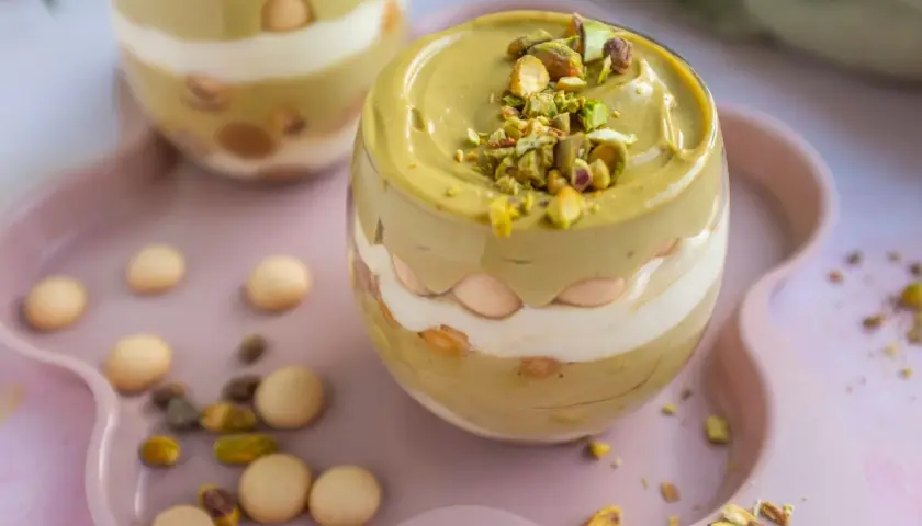 Pyszny deser w pucharku: krem pistacjowy z mascarpone, przełożony biszkoptami i posypany pistacjami.