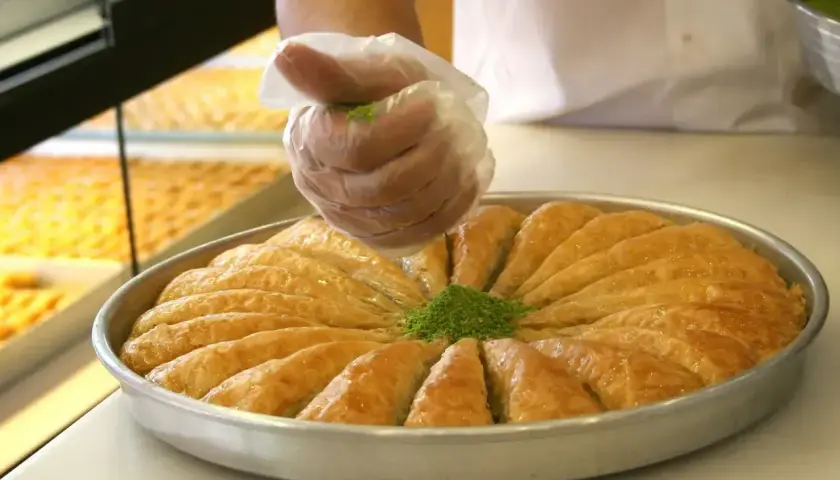 Ręka w rękawiczce posypuje baklavę zielonymi pistacjami. To pyszne ciasto, które warto poznać!