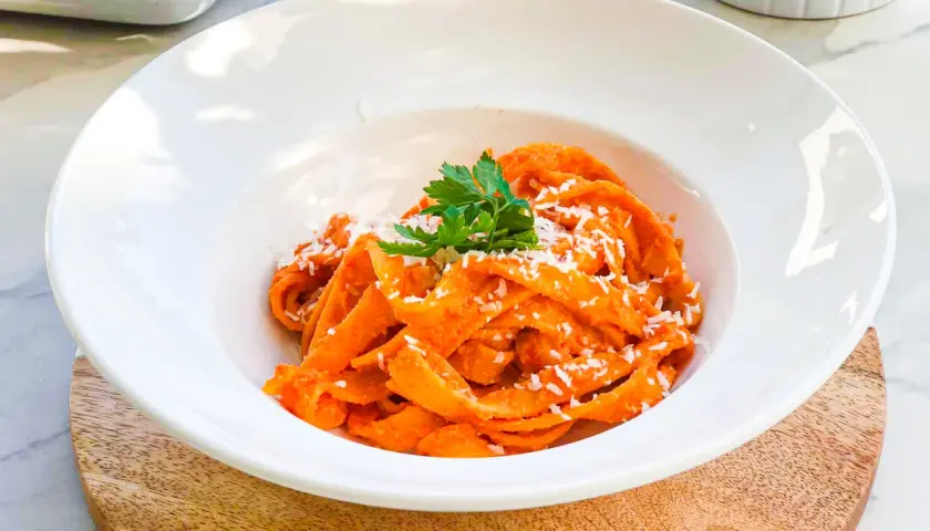 Pappardelle z kremowym sosem z pieczonej papryki, posypane parmezanem i udekorowane natką pietruszki. Pyszne danie, które zachwyca smakiem.