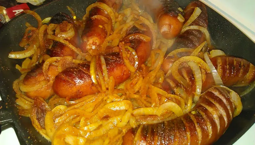 Gorąca kiełbasa z cebulą skwierczy na patelni, tworząc apetyczny aromat.