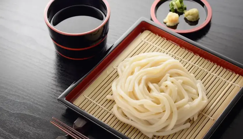 Prosty makaron udon przepis: grube kluski na bambusowej macie, miseczka z sosem i dodatkami. Idealne danie.