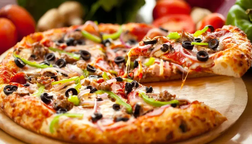 Pyszna pizza z gotowego ciasta, obficie posypana serem, oliwkami, papryką i mięsem. Ser ciągnie się apetycznie.