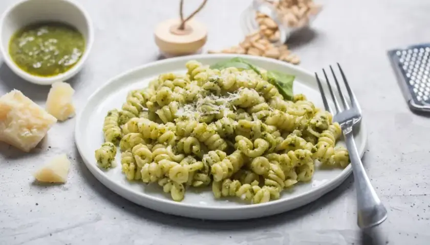 Fusilli z pesto, posypane parmezanem. Na stole kawałek sera, miseczka sosu i słoiczek z orzeszkami pinii. Różne rodzaje makaronu mogą być równie pyszne!