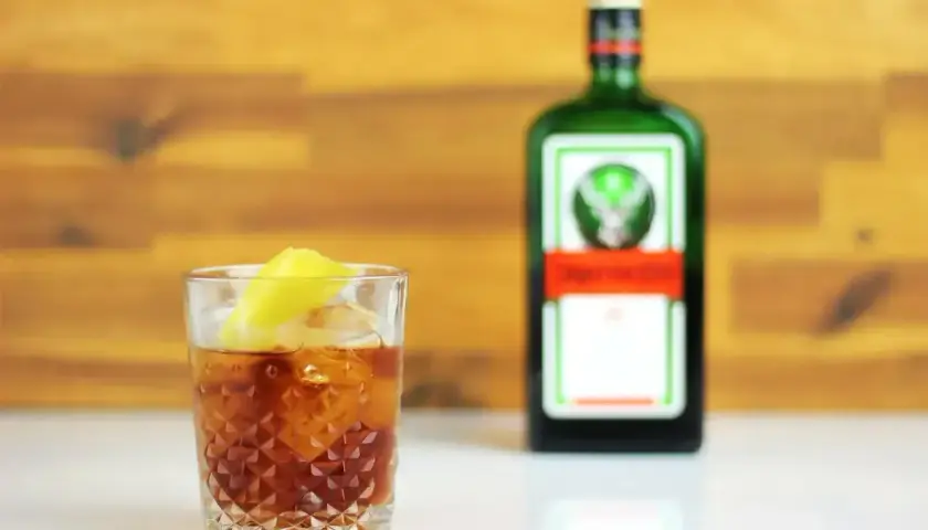 Szklanka z drinkiem i plasterkiem cytryny, obok butelka Jägermeister. Idealny na wieczór z przyjaciółmi, z nutą jagermeister orange.