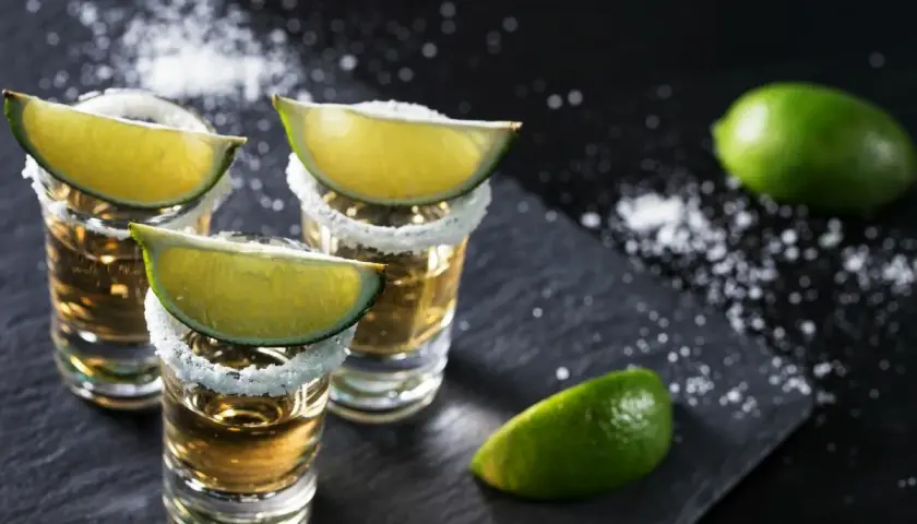 Trzy kieliszki tequili z solą i plasterkami limonki. Idealne z czym pić tequilę, gdy chcesz poczuć smak Meksyku.