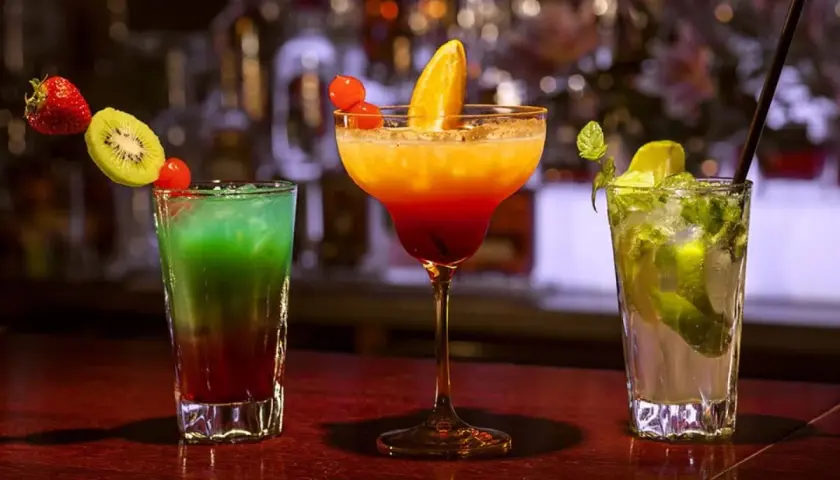 Kolorowe drinki na barze: zielony z kiwi i truskawką, pomarańczowo-czerwony z pomarańczą, oraz mojito z miętą i limonką. Idealne na wieczór z **tekila**.