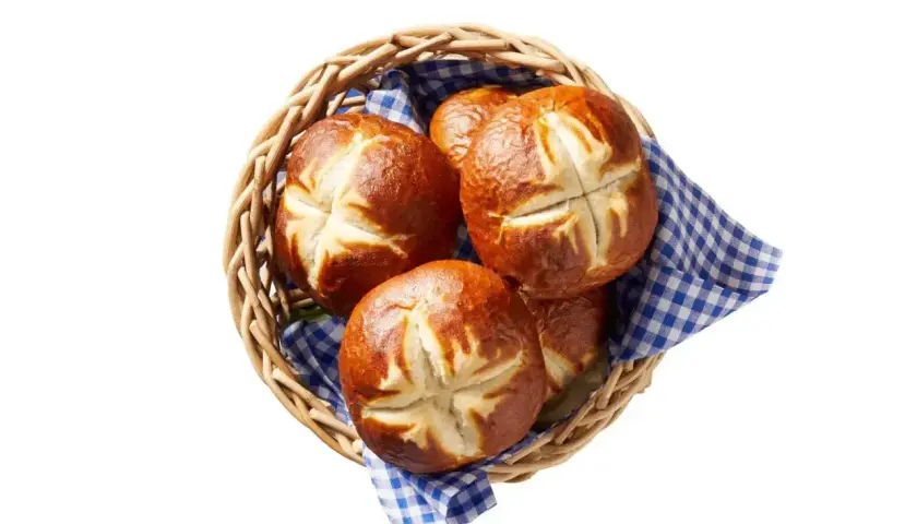 Koszyk z kilkoma świeżymi bułkami bawarskimi, ułożonymi na niebiesko-białej kratkowanej ściereczce.