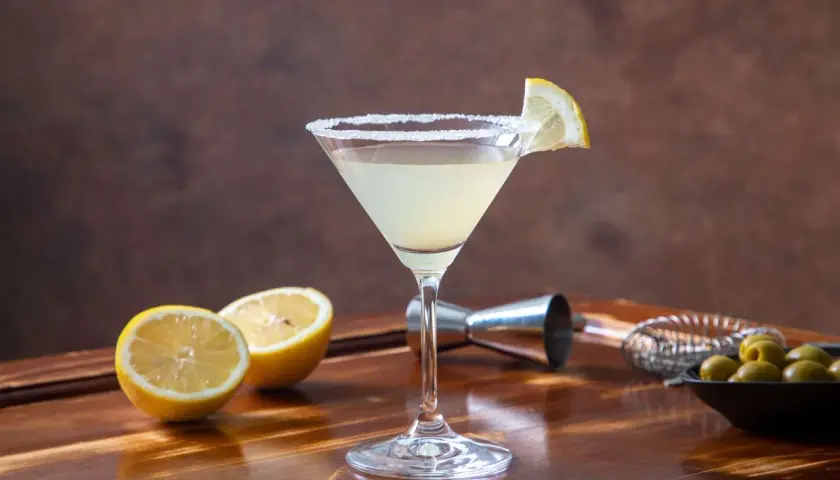 Elegancki drink Martini Bianco z cytryną i solą na kieliszku, obok połówki cytryny i oliwek.
