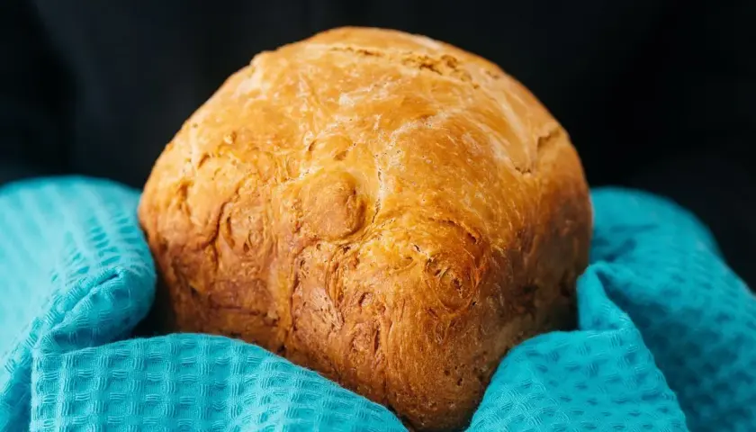 Chleb z airfryer, pachnący i złocisty, owinięty w turkusowy ręcznik. Idealny na śniadanie.