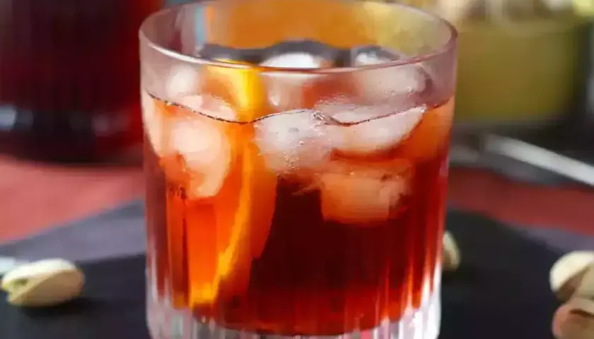 Klasyczny negroni przepis: czerwony koktajl z lodem i pomarańczą w szkle, obok pistacje.