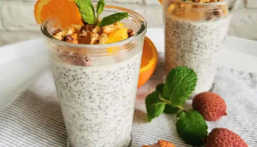 Pudding chia z pomarańczą i orzechami, ozdobiony miętą i owocami lychee.