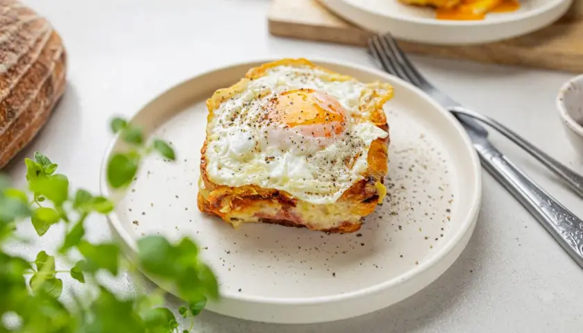 Pyszny croque madame z jajkiem sadzonym na wierzchu, podany na talerzu z pieprzem.