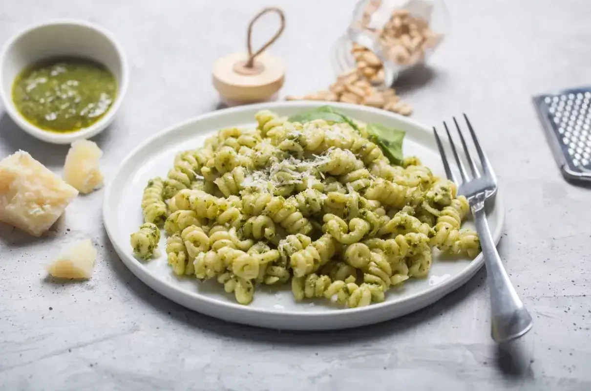Fusilli z pesto, posypane parmezanem. Na stole kawałek sera, miseczka sosu i słoiczek z orzeszkami pinii. Różne rodzaje makaronu mogą być równie pyszne!