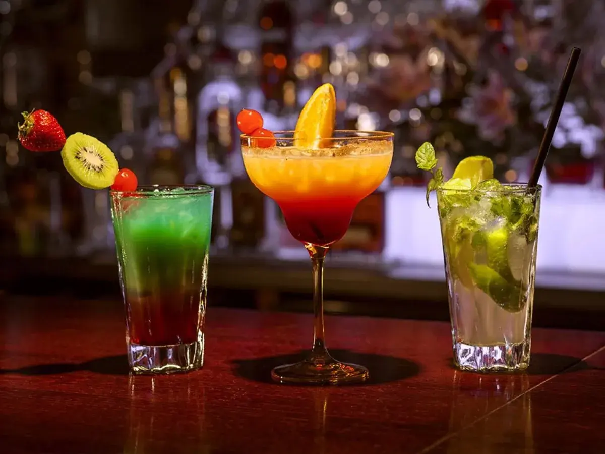 Kolorowe drinki na barze: zielony z kiwi i truskawką, pomarańczowo-czerwony z pomarańczą, oraz mojito z miętą i limonką. Idealne na wieczór z **tekila**.