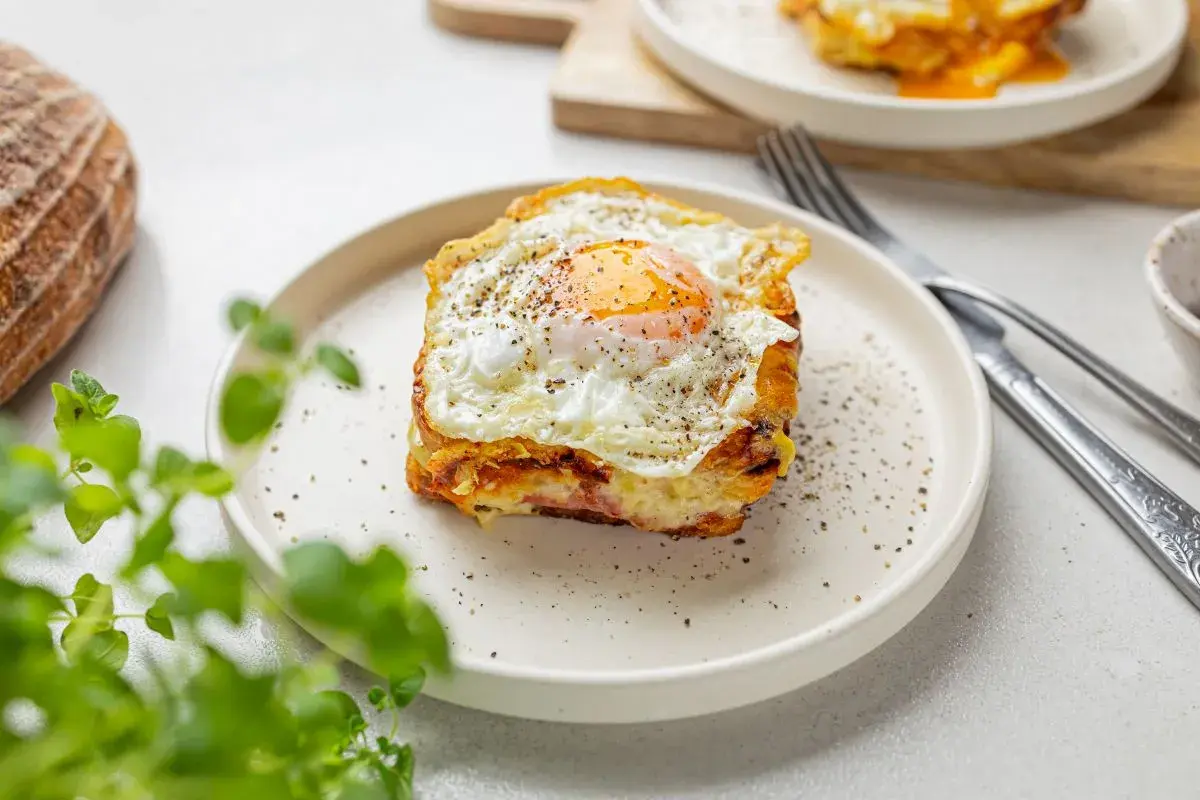 Pyszny croque madame z jajkiem sadzonym na wierzchu, podany na talerzu z pieprzem.