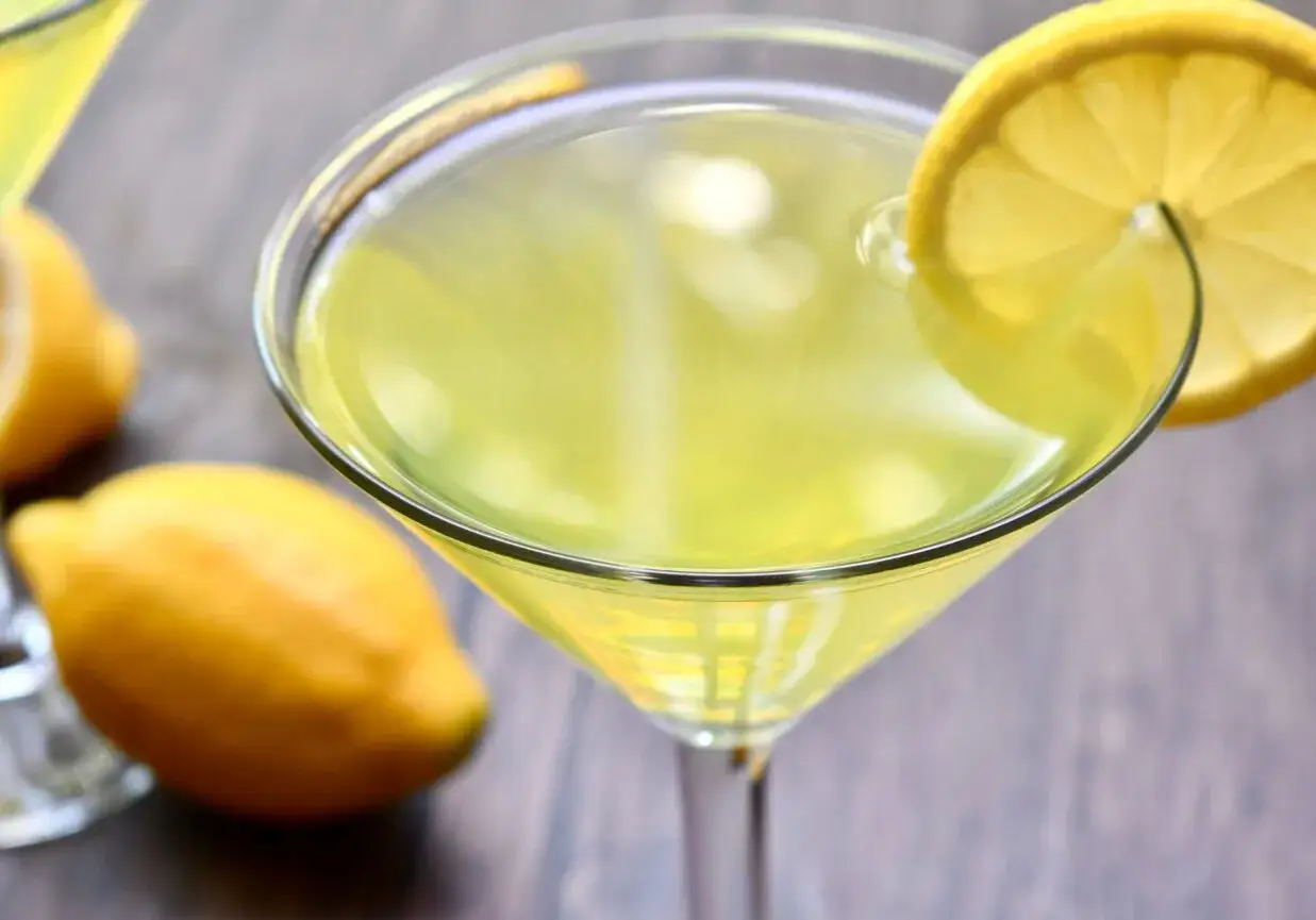 Orzeźwiający drink z limoncello, ozdobiony plasterkiem cytryny, obok leżą świeże cytryny.