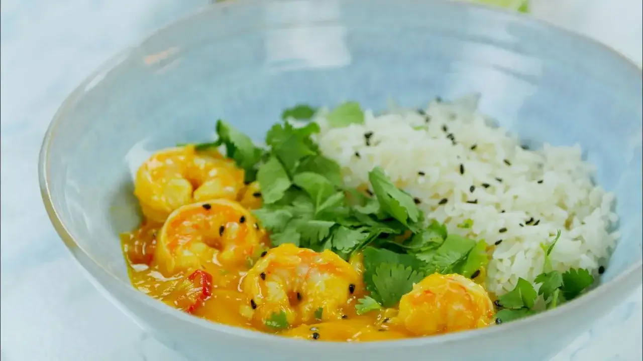 Krewetki z ryżem w sosie curry, ozdobione świeżą kolendrą i czarnym sezamem, podane w niebieskiej misce.