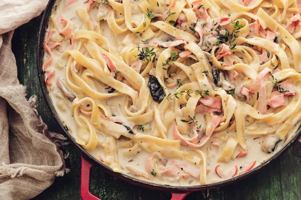 Tagliatelle w kremowym sosie z kawałkami szynki i grzybów, udekorowane świeżym tymiankiem. Pyszny sos do makaronu.
