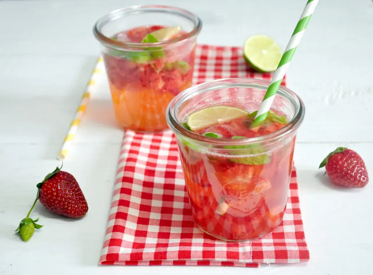 Orzeźwiający drink z truskawkami, miętą i limonką, podany w słoiku z czerwoną serwetką. Idealny na letnie popołudnie.