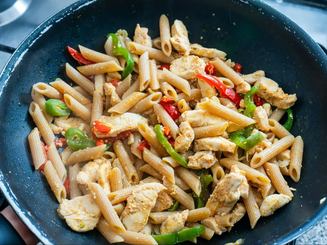 Penne z kurczakiem i kolorową papryką w sosie, danie gotowe do podania.