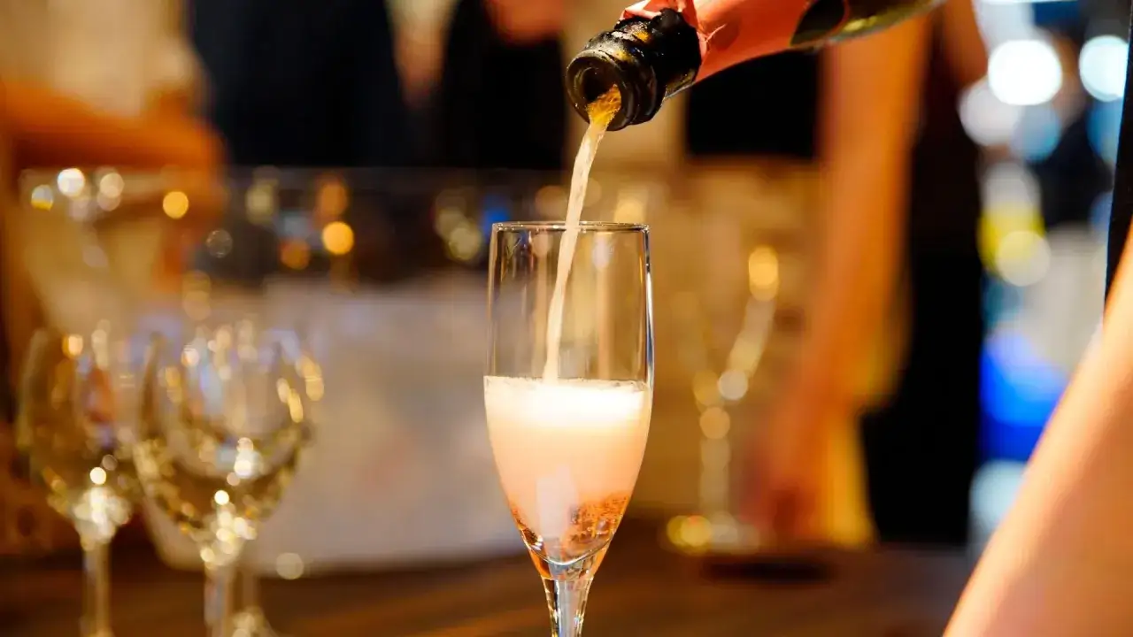 Nalewanie musującego wina cava do kieliszka. W tle widać inne kieliszki i rozmyte światła, sugerujące uroczystą atmosferę.