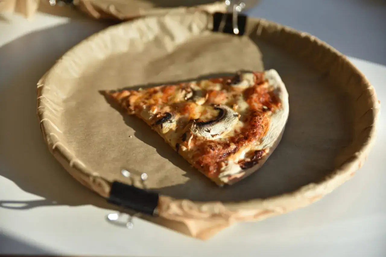 Kawałek pizzy z pieczarkami na brązowym papierze. Zastanawiasz się, ile waży kawałek pizzy?