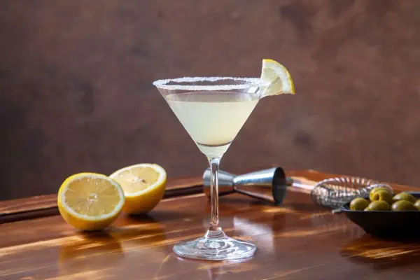 Elegancki drink Martini Bianco z cytryną i solą na kieliszku, obok połówki cytryny i oliwek.